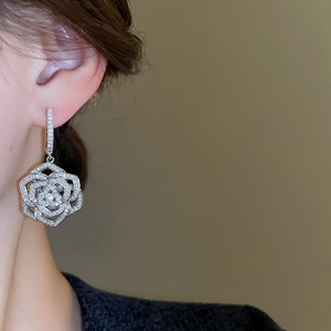 Close-up of sparkling silver zircon flower earrings on ear with layered floral design
