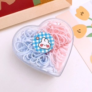 Macro shot of colorful pastel hair ties in a heart-shaped clear storage box with tulips