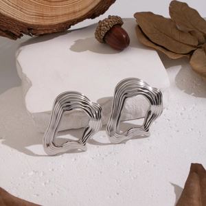 Close-up of irregular silver fluid metal earrings on a natural stone and wood background