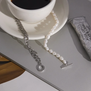 Detail view of silver curb chain and baroque pearl bracelet set by white coffee cup