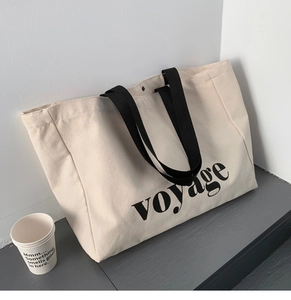 Close-up of cream canvas tote bag featuring black voyage text and sturdy shoulder straps