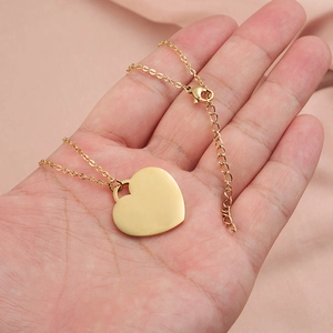 Golden stainless steel heart pendant necklace worn on neck with pink fabric backdrop