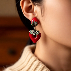 Macro view of vintage red heart strawberry earrings with gold leaf detail on beige sweater