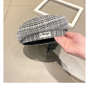 Detailed close-up of a black and white houndstooth beret with a retro woven label