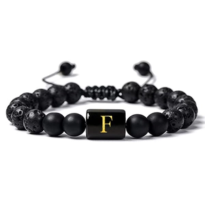 Gros plan du bracelet réglable en pierre de lave avec une lettre F dorée sur une perle noire