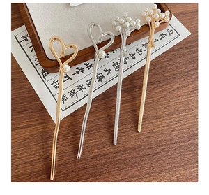 Detailed view of metal hairpins with pearls and heart designs on a wooden tray