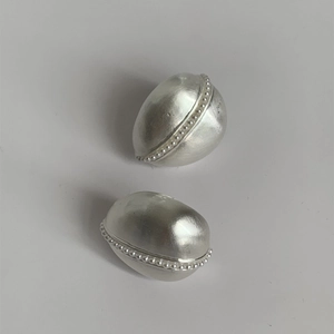 Dettaglio macro di orecchini a goccia in argento con finitura spazzolata e bordi perlati