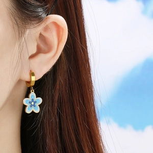 Goldene Blumenohrringe mit blauem Emaille-Anhänger, getragen von einem Model vor blauem Himmel