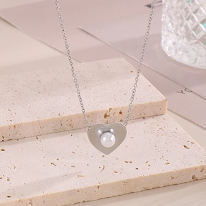 Detail of silver heart necklace with pearl inlay on minimalist stone pedestal