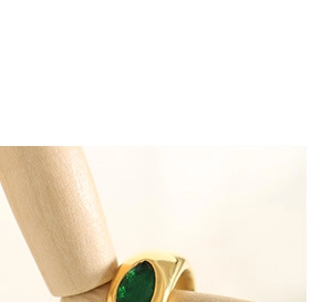 Close-up of a wide gold ring featuring an oval green gemstone on a wooden display