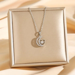 Silver crescent moon and heart pendant necklace with zircons on a golden jewelry box