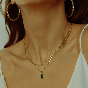 Close-up of gold layered necklaces with a green gemstone drop pendant and twisted hoop earrings