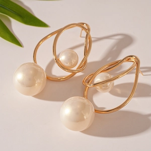 Detail of elegant gold metal wire wrapped earrings with two white pearls on beige surface