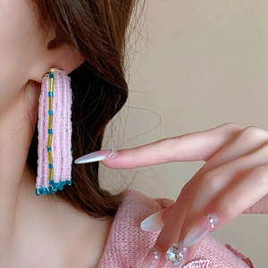 Gros plan de boucles d'oreilles pompons en perles roses et turquoise sur un mannequin