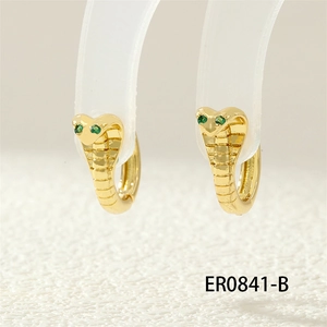 Macro shot of gold cobra hoop earrings with green stone eyes on a clear stand