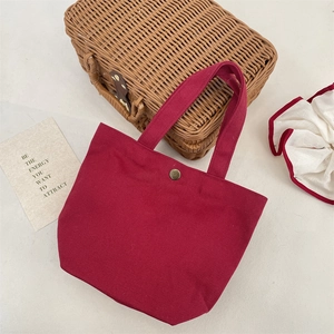 Detail of burgundy canvas tote bag featuring vintage metal snap button and woven texture