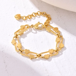 Detail of gold chain bracelet with heart charms and secure lobster clasp on stone surface