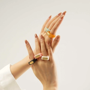 Close-up of five colorful resin square rings with gold metal inlay shown on a hand