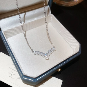 Macro detail of V-shaped silver necklace with white pearls and zircons in a jewelry box