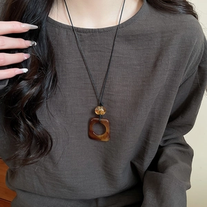 Detail of square amber leopard print resin pendant on black cord necklace worn by a model