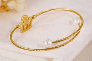 Close-up of golden twisted metal bracelet with elegant crown and white pearl details