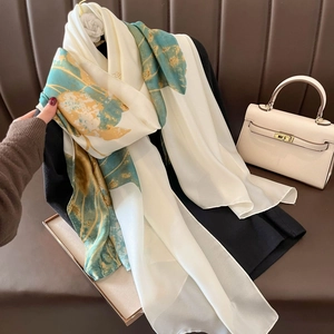 Elegant white silk scarf with green and yellow floral patterns on a leather sofa backdrop
