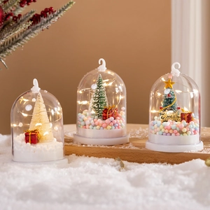 Three glowing Christmas snow globes with mini trees and warm LED lights on a wooden stand
