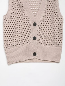 Close-up of beige knit vest featuring intricate hollow crochet texture and black buttons
