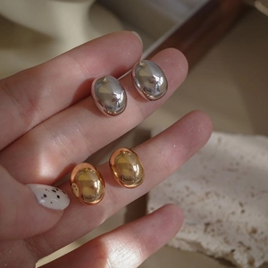 Detailed view of glossy gold and silver minimalist metal stud earrings held by a model