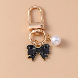 Elegant pearl keychain with black enamel bow and golden lobster clasp on beige background