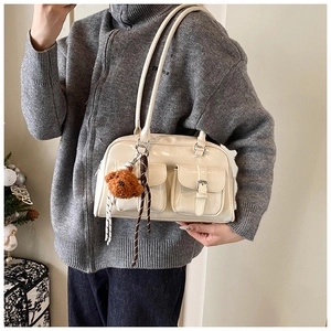 Close-up of a white PU leather pillow bag with dual front pockets and brown bear charm