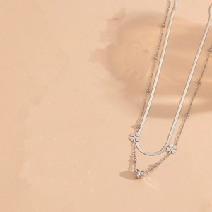Detail of silver stainless steel double layer necklace with clover pendants and beads