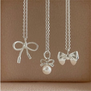 Detailed view of three 925 sterling silver bow pendants with pearls on a beige velvet
