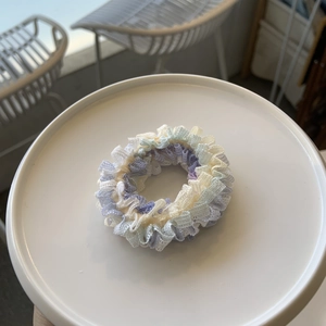 Détail d'un chouchou en dentelle multicouche bleu pastel et lavande sur un plateau