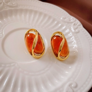 Close-up of orange resin droplet earrings with golden metal frames on a ceramic plate
