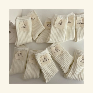 Flat lay of multiple cream-colored ribbed wool socks with brand labels on white background