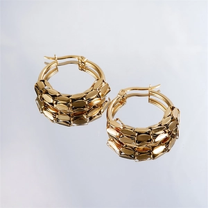 Detail view of gold hoop earrings with textured scale design on a reflective surface