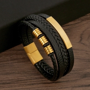Close-up of multi-layer black braided leather bracelet with golden metal buckle and charms