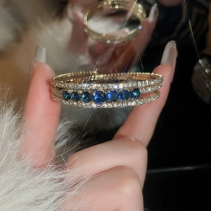 Detail of multi-layered gold bracelet with sparkling zircon and blue gemstone accents