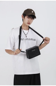 Close-up of black crocodile texture box bag with adjustable strap worn by model