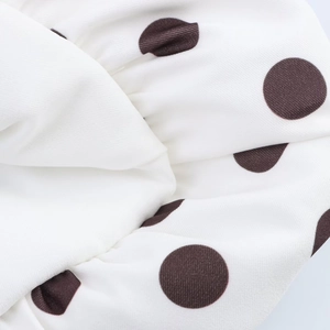 Gros plan sur un tissu en sergé blanc à pois marron foncé avec une texture plissée douce