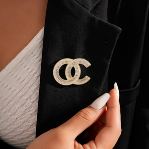 Detailed close-up of a 14k gold-plated twisted brooch with cubic zirconia and pearls on a blazer