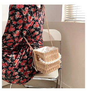 Detail of woven straw bucket bag featuring a pearl handle and gold chain strap on a chair