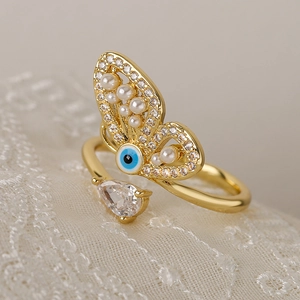 Gold butterfly ring with evil eye design, pearls and pear-shaped zircon on lace background