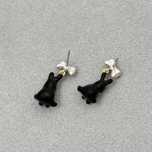 Detail showing 3D black enamel rabbit earrings with silver bowknots on felt surface