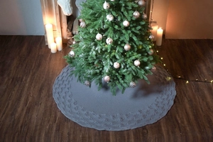 Close-up of grey knitted Christmas tree skirt with spider pattern texture in home setting