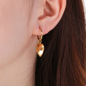 Close-up of polished gold heart pendant earring worn by a model for a stylish modern look