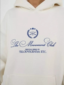 Close-up of the blue letter print and badge logo on this cream oversized hoodie top
