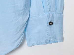 Detailed close-up of light blue cotton linen shirt cuff with dark brown button