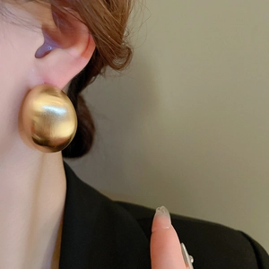 Close-up of a large gold geometric spherical earring with a brushed metal finish on model